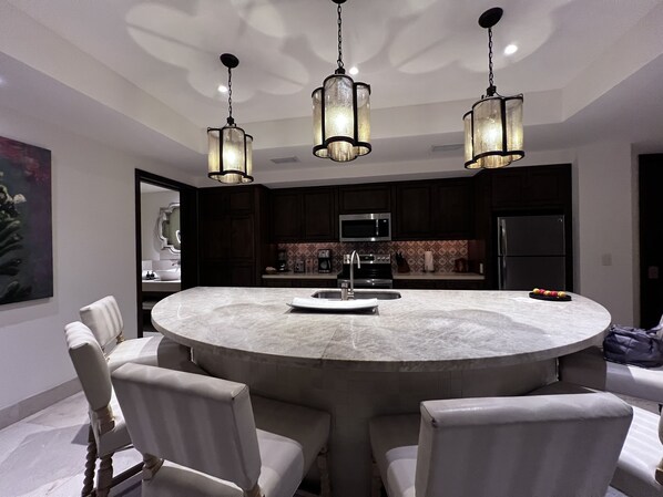 A modern kitchen with dark cabinetry, a central island with seating, and pendant lighting.