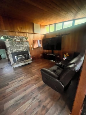 Ein Wohnzimmer mit Kamin aus Stein, einer schwarzen Ledersofa und einem flachbildfernseher an der Wand.