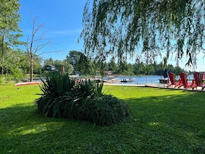 A lakeside outdoor area with a dock, red chairs, and a grassy lawn. - Private Georgian Bay Waterfront Cottage: Dock, Sand Beach, Hot Tub, Dogs OK (Tay)