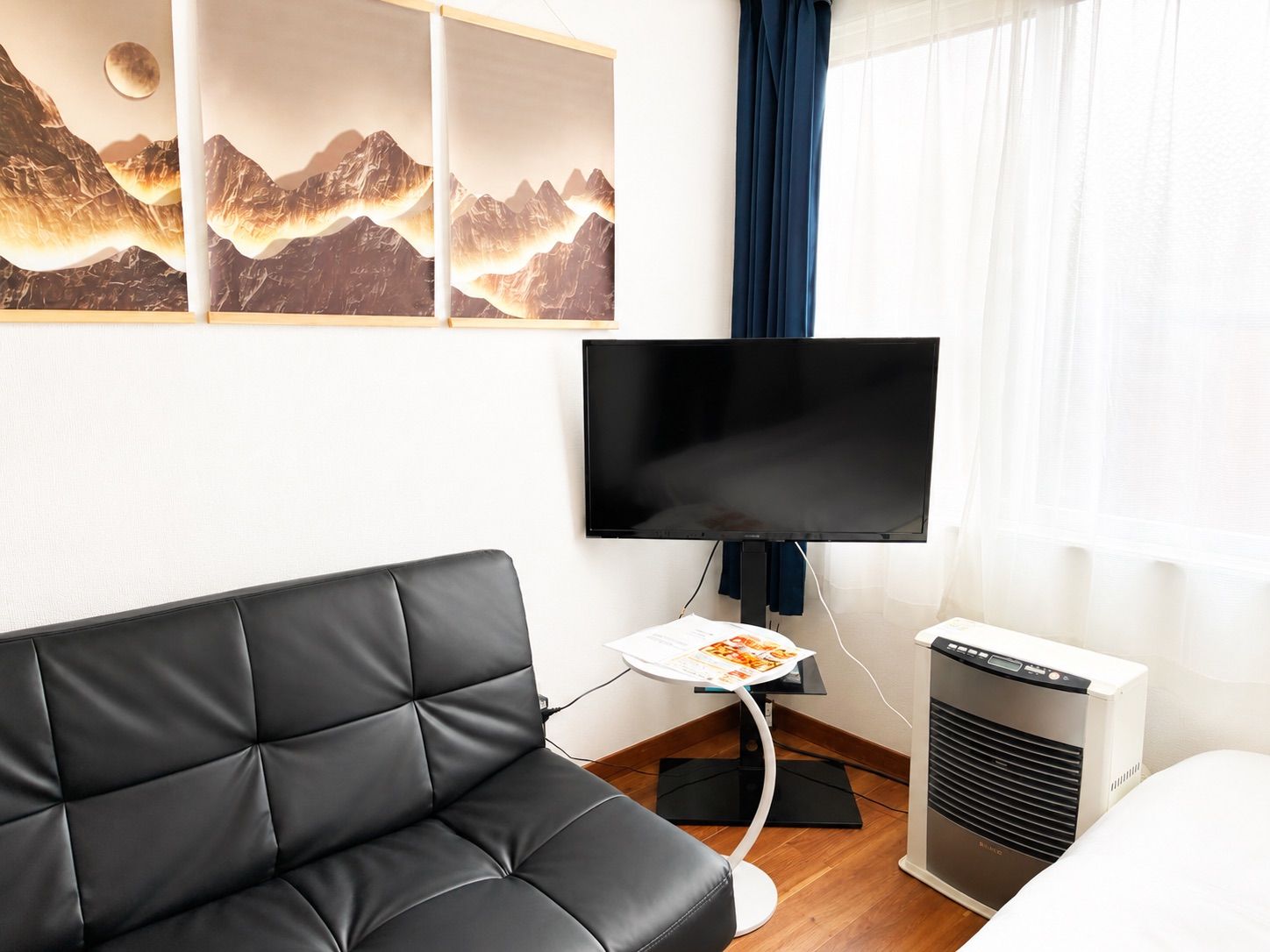 Une chambre d’hôtel moderne avec un canapé en cuir noir, un téléviseur à écran plat fixé au mur et un radiateur au sol.