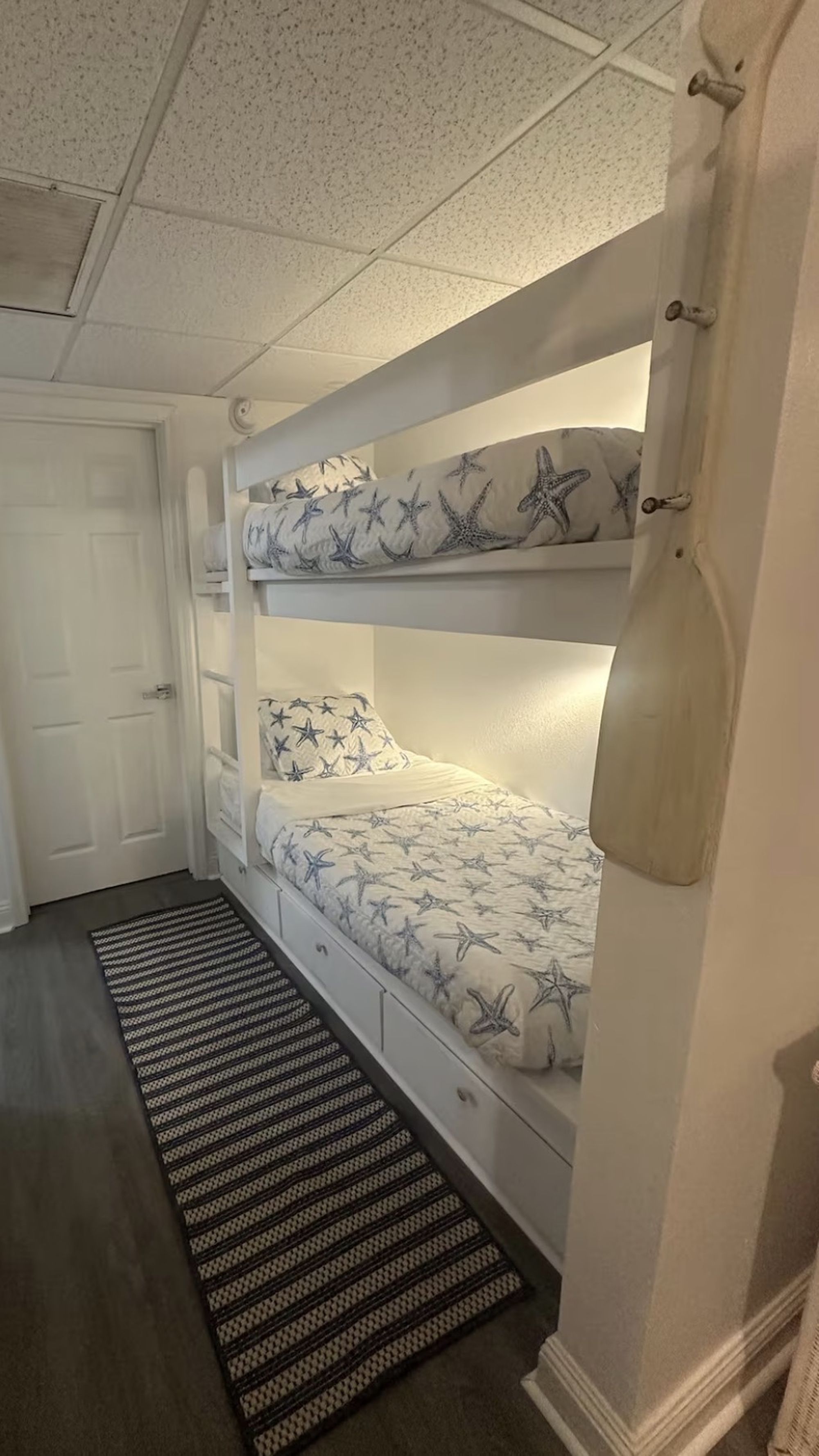 A bunk bed with starfish bedding, a white door, and a patterned rug.
