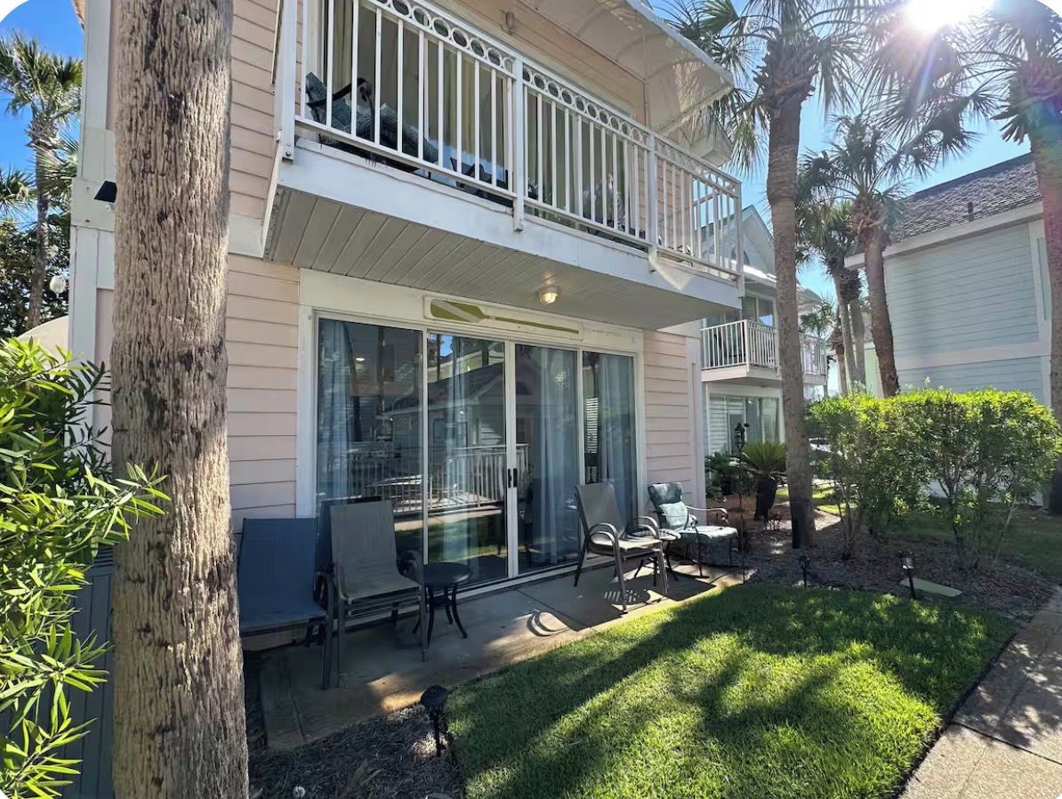 A two-story house with a balcony, a patio with outdoor furniture, and a well-maintained lawn.