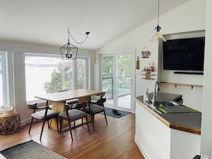 A modern kitchen with a dining area, large windows, and a TV mounted on the wall. - Charming Lakeside Cottage (North Bay)