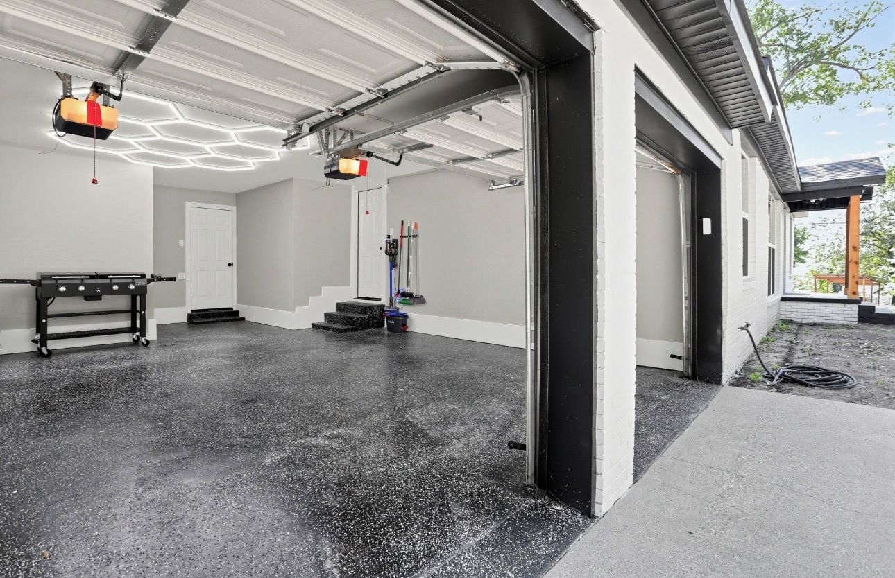 Ett garage med ett betonggolv, ett tak med sexkantig belysning och en dörr som leder ut till ett takförsett utomhusområde.
