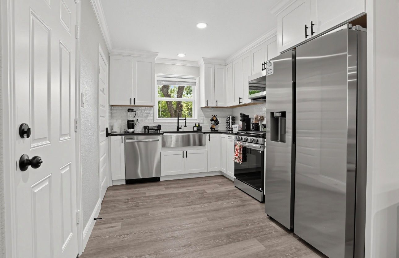 Una cocina moderna con armarios blancos, electrodomésticos de acero inoxidable y un ventanal que proporciona luz natural.