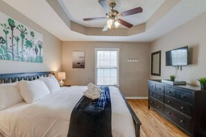 A hotel room with a bed, a ceiling fan, a window with blinds, a dresser, and a television on the wall. - Modern Nashville Getaway (Nashville)