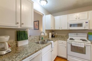 A kitchen with white cabinets, a granite countertop, a stainless steel sink, a microwave, a stove, and a dishwasher. - Modern Nashville Getaway (Nashville)