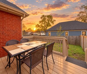 A wooden deck with a table and chairs, a brick wall, and a view of a house and trees. - Big Backyard | Mins to Downtown | 3BR Sleeps 8 (Nashville)