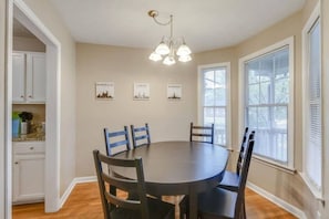 A dining room with a round table, six chairs, a chandelier, and cityscape wall art. - Modern Nashville Getaway (Nashville)