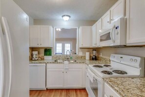 A compact kitchen with white cabinets, a granite countertop, a stove, and a microwave. - Big Backyard | Mins to Downtown | 3BR Sleeps 8 (Nashville)