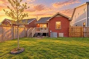 A residential backyard with a wooden deck, a small tree, and a grassy lawn. - Modern Nashville Getaway (Nashville)