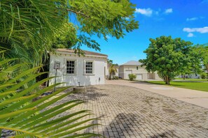 A residential property with a paved driveway, a white building with a tiled roof, and a well-maintained lawn. - Riverfront 5BR Villa - Private Dock & Pool (Fort Myers)