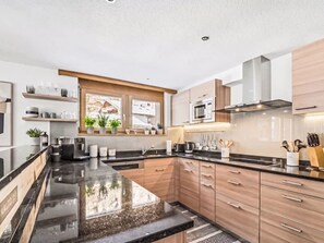 A modern kitchen with a black countertop, wooden cabinets, and a window with plants. - Kanzi, St. Anton by Interhome (Sankt Anton am Arlberg)