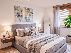 Une chambre à coucher moderne avec un grand lit, des tables de chevet, un miroir et un tableau au mur.