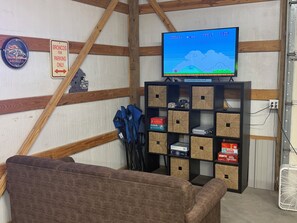 A room with a television displaying a video game, a couch, and a shelf with various items. -  Shed in Great Bend perfect for your next fun gathering. (Great Bend)