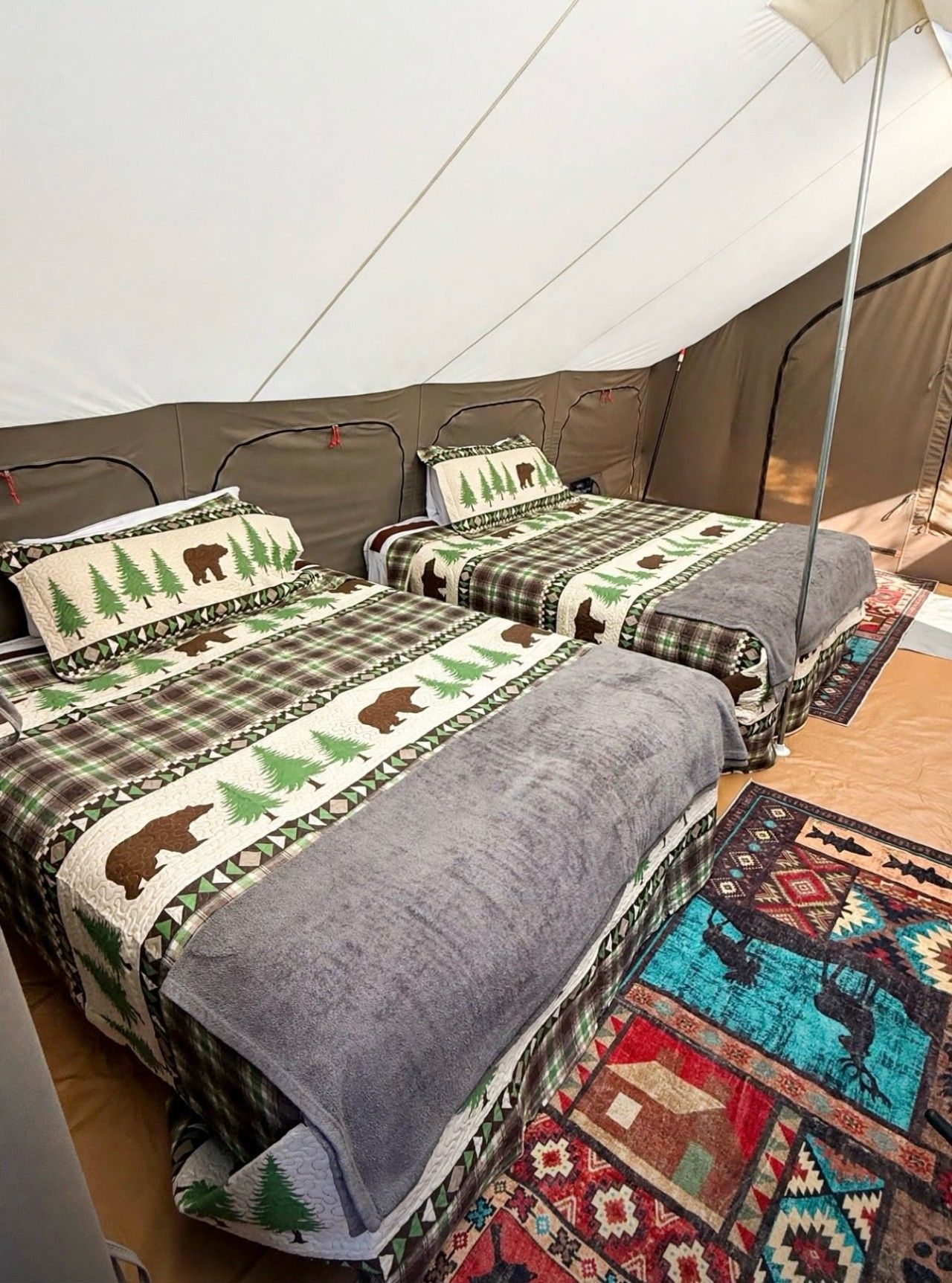 A tent with two beds, each with a blanket and pillow featuring a forest and bear design.