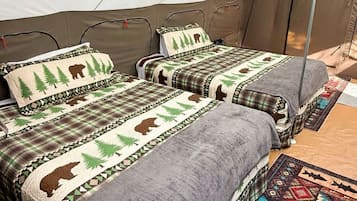 A tent with two beds, each with a blanket and pillow featuring a forest and bear design.