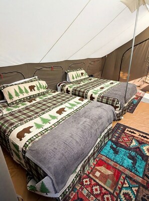 A tent with two beds, each with a blanket and pillow featuring a forest and bear design.