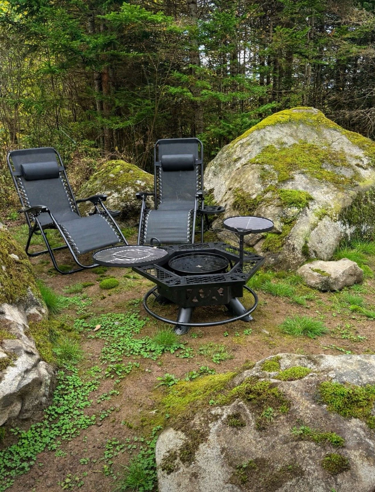 Een camping met twee zwarte loungestoelen, een klein rond tafeltje en een draagbare barbecue.