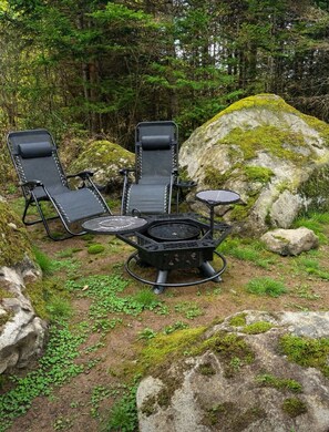 Een camping met twee zwarte loungestoelen, een klein rond tafeltje en een draagbare barbecue.