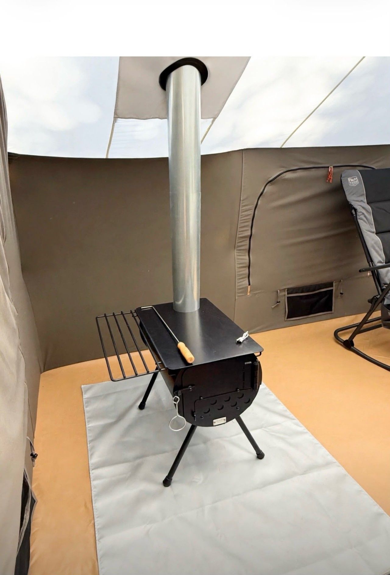 A portable stove with a chimney, a grill, and a folding chair on a rooftop.