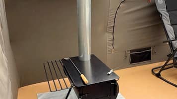 A portable stove with a chimney, a grill, and a folding chair on a rooftop.