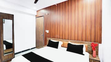 A hotel room with a wooden headboard, a bed with black and white bedding, a nightstand with a vase of red flowers, and a ceiling fan.