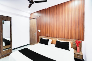 A hotel room with a wooden headboard, a bed with black and white bedding, a nightstand with a vase of red flowers, and a ceiling fan.