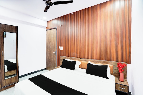 A hotel room with a wooden headboard, a bed with black and white bedding, a nightstand with a vase of red flowers, and a ceiling fan.