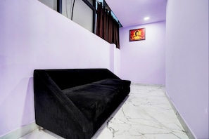 A room with a black sofa against a purple wall, a marble floor, and a Buddha statue on the wall. - Super Collection O Hotel Star Inn Near (Ghaziabad)