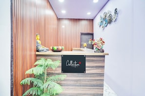 A reception desk with a sign that reads 'Collection,' a Buddha statue, a decorative bowl, and a potted plant.