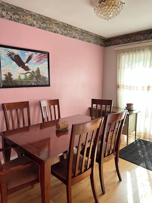 Uma sala de jantar com mesa e cadeiras de madeira, um quadro emoldurado de uma águia e um lustre.