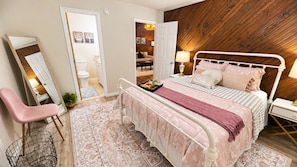 Un dormitorio con cama, mesita de noche, lámpara, silla y espejo.