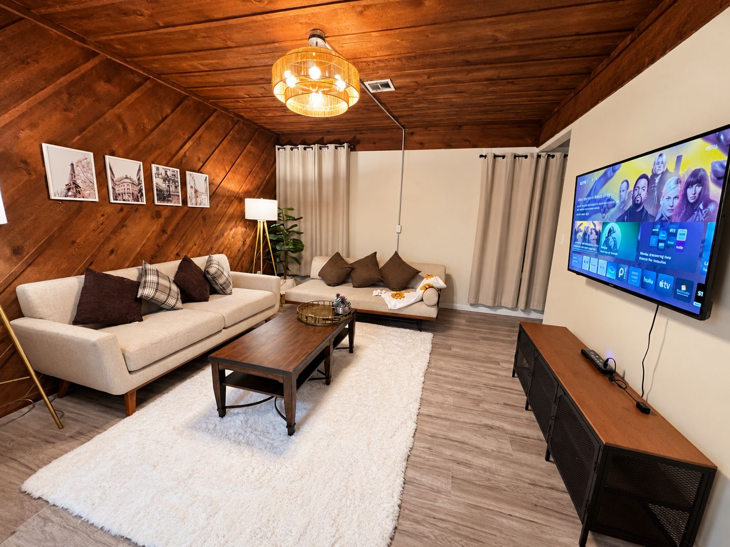 A modern living room with a wooden ceiling, two sofas, a coffee table, a TV, and framed pictures on the wall.