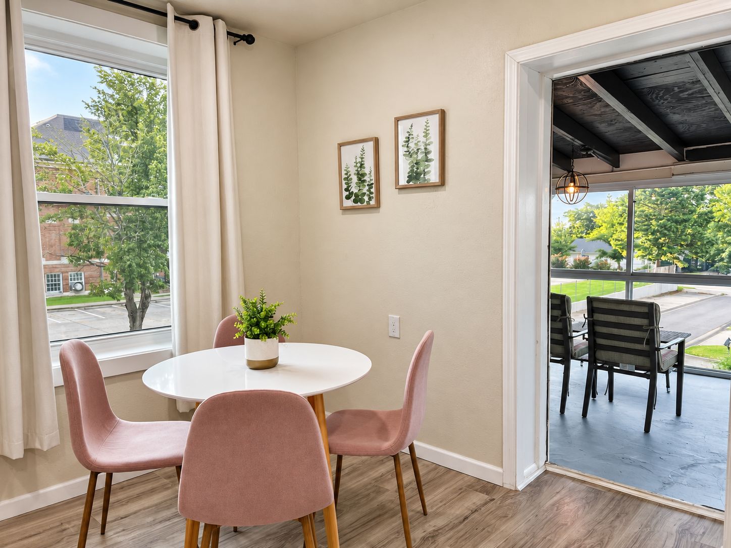 Un coin repas avec une table ronde, quatre chaises, une plante en pot et deux tableaux encadrés au mur.