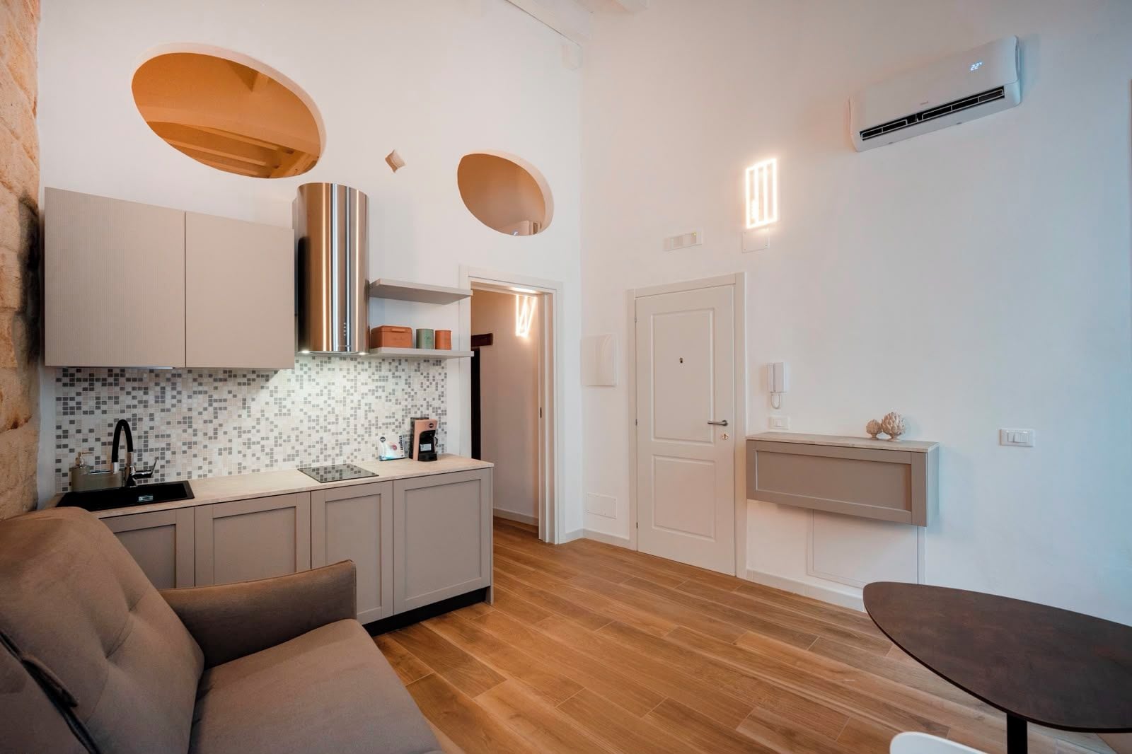 Cocina compacta de diseño moderno, con horno empotrado, cafetera y una pequeña encimera.