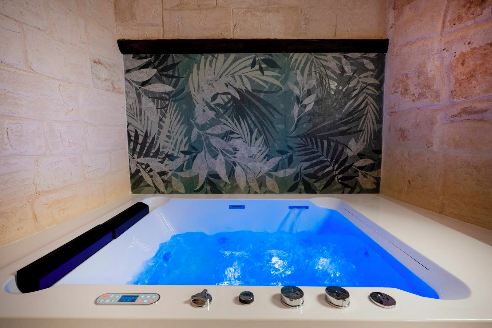 A hot tub with a control panel, surrounded by brick walls and a leaf-patterned backdrop.
