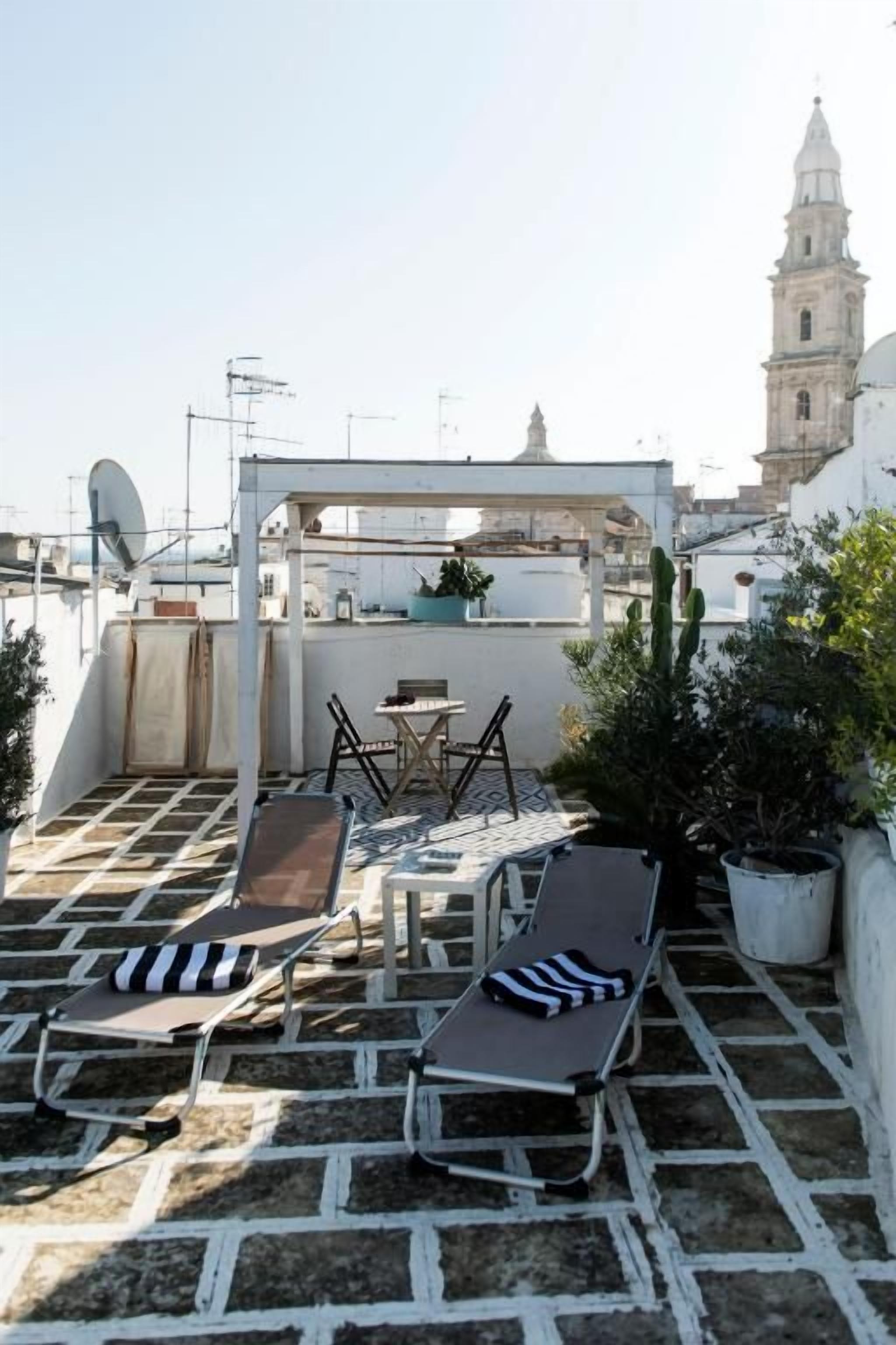 A rooftop terrace with lounge chairs, a table, and potted plants.