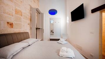 A hotel room with a bed, a flat-screen TV, a mirror, and a towel rack.