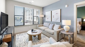 A modern living room with a sofa, coffee table, TV, and artwork on the wall. - Landing | Incredible 1BD, Courtyard, Clubhouse (Fort Wayne)