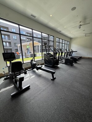 A gym with exercise equipment, large windows, and a view of buildings outside. - Landing | Chic 1BD, Clubhouse, Courtyard (Fort Wayne)