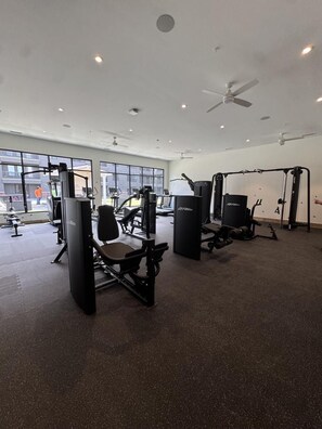 A gym with various exercise machines, large windows, and ceiling fans. - Landing | Spectacular 1BD, Clubhouse, Courtyard (Fort Wayne)