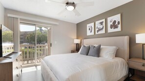 A hotel room with a large bed, a ceiling fan, a TV, and a balcony with a view of the outside. - Landing | Beautiful 1BD, Courtyard, Clubhouse (Fort Wayne)