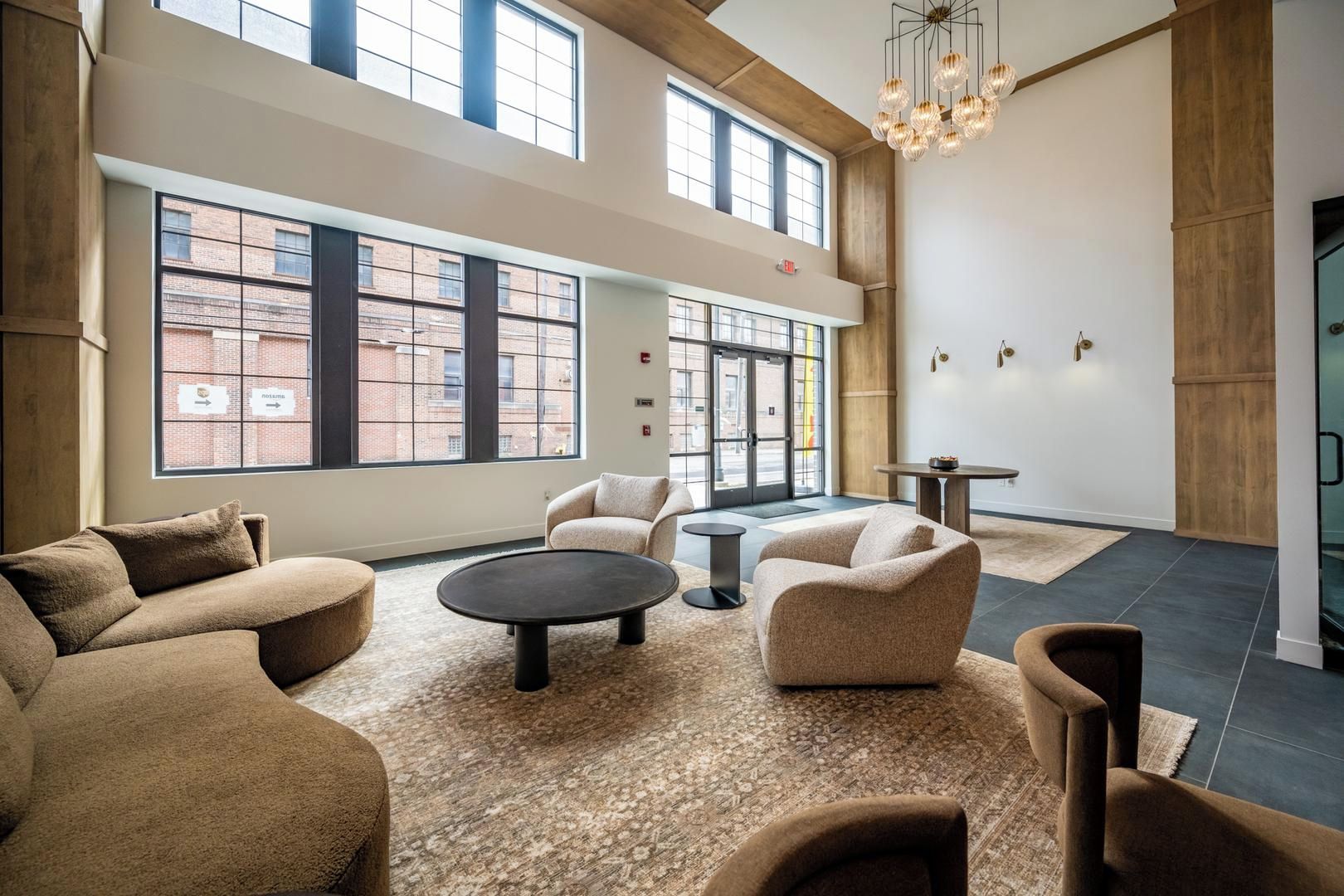 A spacious lounge area with multiple seating options, large windows offering views of the city, and a modern chandelier.