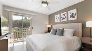 A hotel room with a large bed, a ceiling fan, a TV, and a balcony with a view of the outside. - Landing | Incredible 1BD, Clubhouse, Courtyard (Fort Wayne)