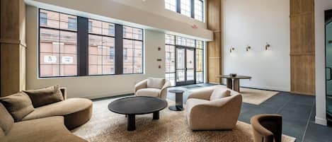 A spacious lounge area with multiple seating options, large windows offering views of the city, and a modern chandelier.