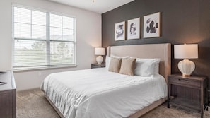 A bedroom with a large bed, two bedside tables, a window with blinds, and three wall-mounted artworks. - Landing | Chic 2BD, Courtyard, Clubhouse (Fort Wayne)