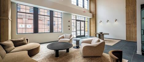 A spacious lounge area with multiple seating options, large windows offering views of the city, and a modern chandelier.