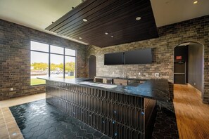 A modern kitchen with a large island, dark wood ceiling, and a brick wall. - Landing | Chic 2BD, Courtyard, Clubhouse (Fort Wayne)