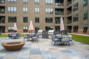 An outdoor patio with a barbecue grill, seating area, and umbrellas. - Landing | Chic 2BD, Courtyard, Clubhouse (Fort Wayne)